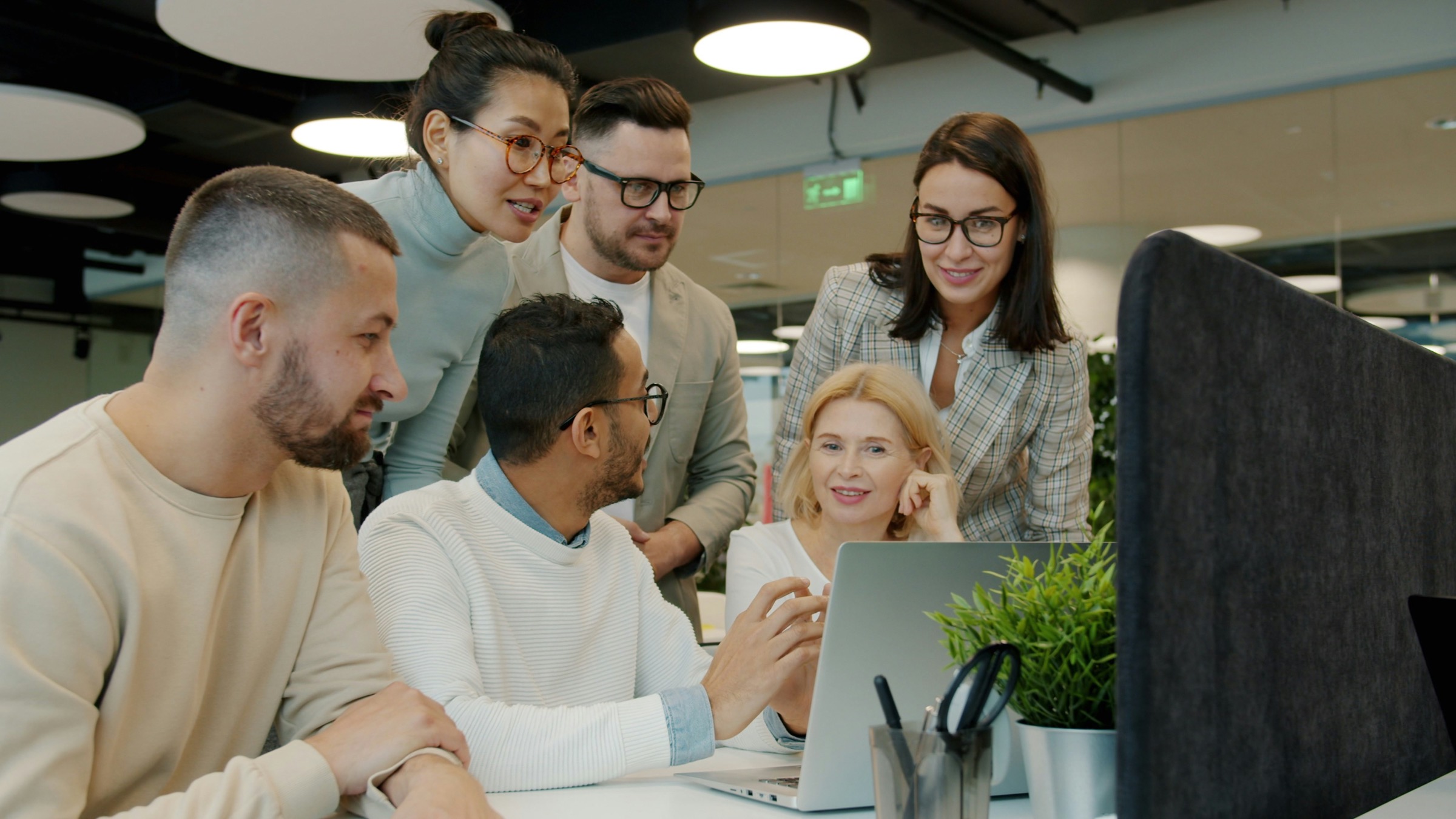 A team of colleagues gathered around a laptop in an office, looking at the screen together.